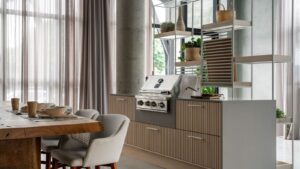 Cozinha moderna e minimalista com uma churrasqueira de inox embutida em um móvel de linhas retas e detalhes em madeira clara. O ambiente conta com prateleiras abertas e plantas decorativas. A mesa de jantar de madeira rústica está disposta ao lado, criando uma atmosfera aconchegante e contemporânea.