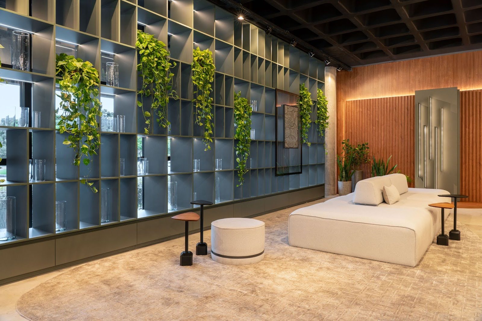 Cozinha contemporânea com ilha central azul clara, três banquetas com assento branco e pés de madeira, armários superiores e inferiores, prateleira suspensa com utensílios e iluminação natural por grandes janelas com cortinas brancas.