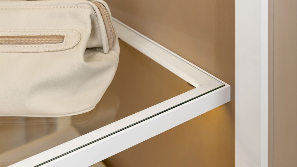 Detalhe de prateleira de vidro com moldura de alumínio branco em closet planejado de luxo, destacando acabamento interno e organização com bolsa de couro.