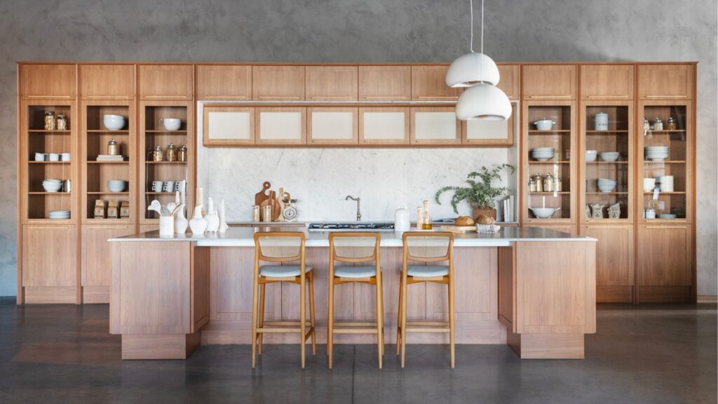 Cozinha planejada moderna com armários de madeira clara, bancada de mármore branco com banquetas e iluminação pendente minimalista.