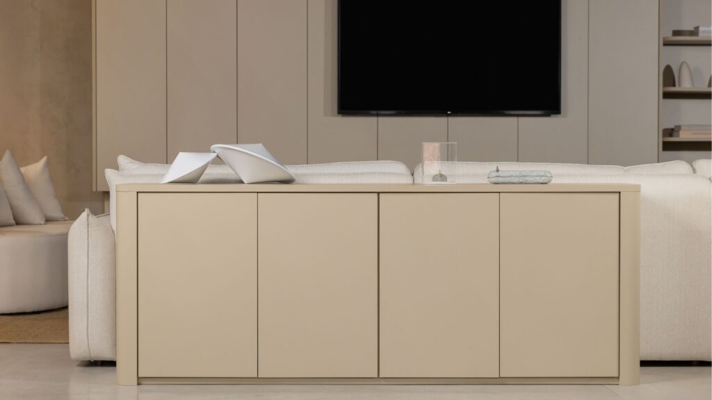 Buffet aparador em tom bege posicionado atrás de sofá off-white em sala de estar moderna com painel de TV ripado ao fundo.